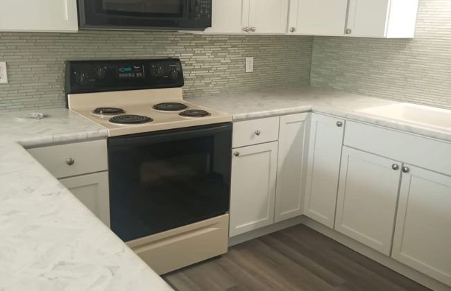 Renovated kitchen with white shaker cabinets, glass tile backsplash, and a black electric range
