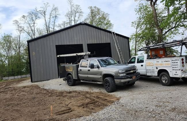 Gray metal garage building with two black overhead doors and two work trucks parked in front