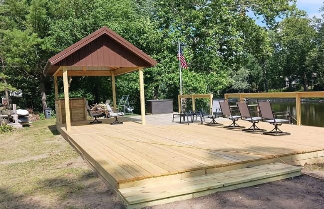 New wood deck with a covered pavilion and lawn chairs on a landscaped lot