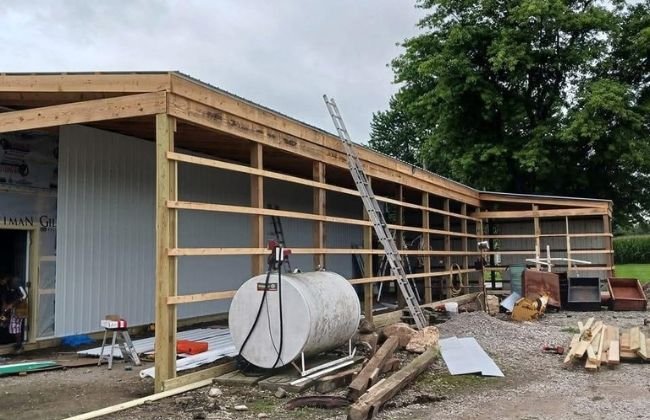 Wood-framed lean-to addition under construction with a ladder and lumber on site