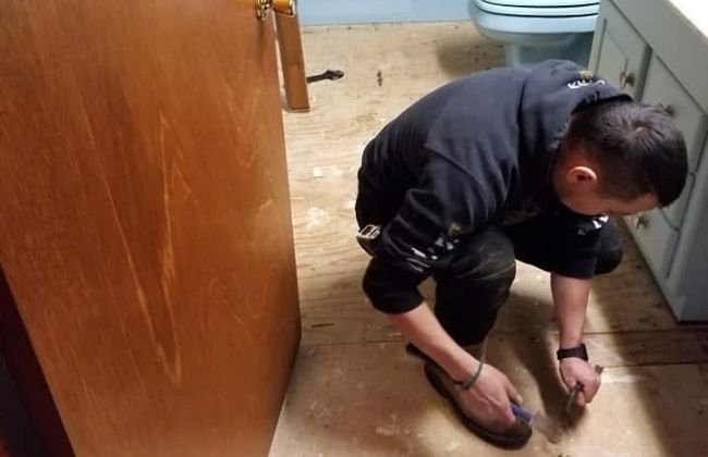 Contractor kneeling on a bathroom floor next to a wood cabinet during an interior renovation