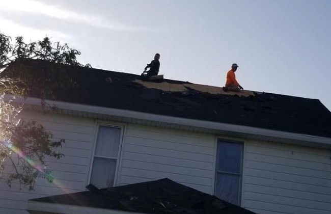 Two roofers working on the roof of a house under a blue sky